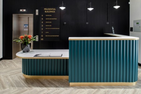 Prudential Buildings, Bristol - reception area with teale wooden panelling on desk, dark wooden panelling behind and light wooden floor. Lift behind desk and red flowers in vase on desk