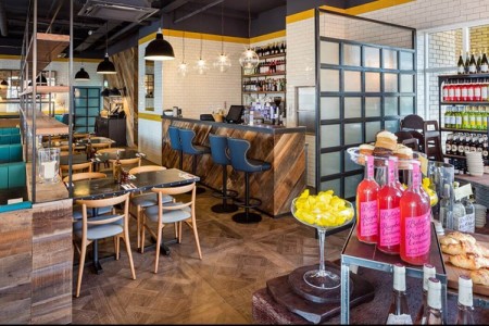 Wildwood, Braintree - bottles on wooden table to the right, dining area ahead with wooden dividers between tables, wooden parquet style floor, bar seating and bar area