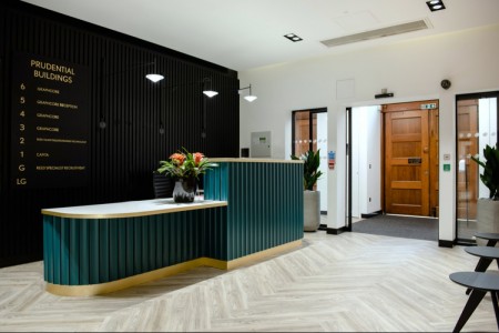 Prudential Buildings, Bristol - light wooden floor, seating area with small tables, teale reception desk, black panelling behind desk with floor numbers on, black vase on desk with red and green flowers