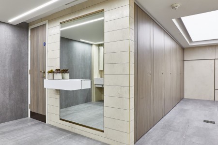 Princesshay Shopping Centre public toilets, Exeter - beige tiling on walls, large floor length mirror with shelf and plants, grey floor tiling, wooden doors on stalls 