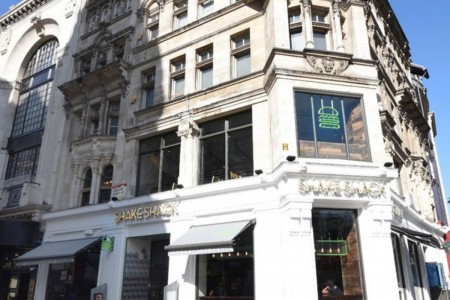 Shake Shack, Leicester Square - white exterior of building with gold branding and neon burger sign in window