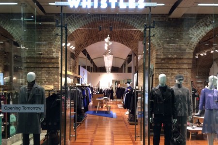 Whistles, St Pancras Station, London - large glass shopfront with wooden floor inside, mannequins and clothing displays visible, brick arches 