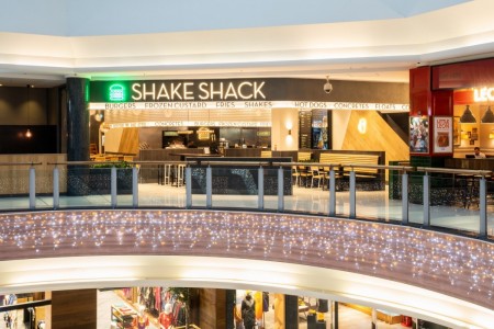 Shake Shack, Brent Cross Shopping Centre, London - exterior, black and white logo with green neon burger on sign, wooden bench seating inside